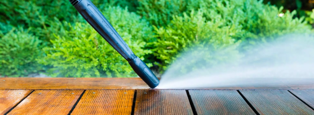 Høytrykksvasker renser en treterrasse, som effektivt fjerner smuss og gjenoppretter treets naturlige skjønnhet mot en frodig hagebakgrunn.