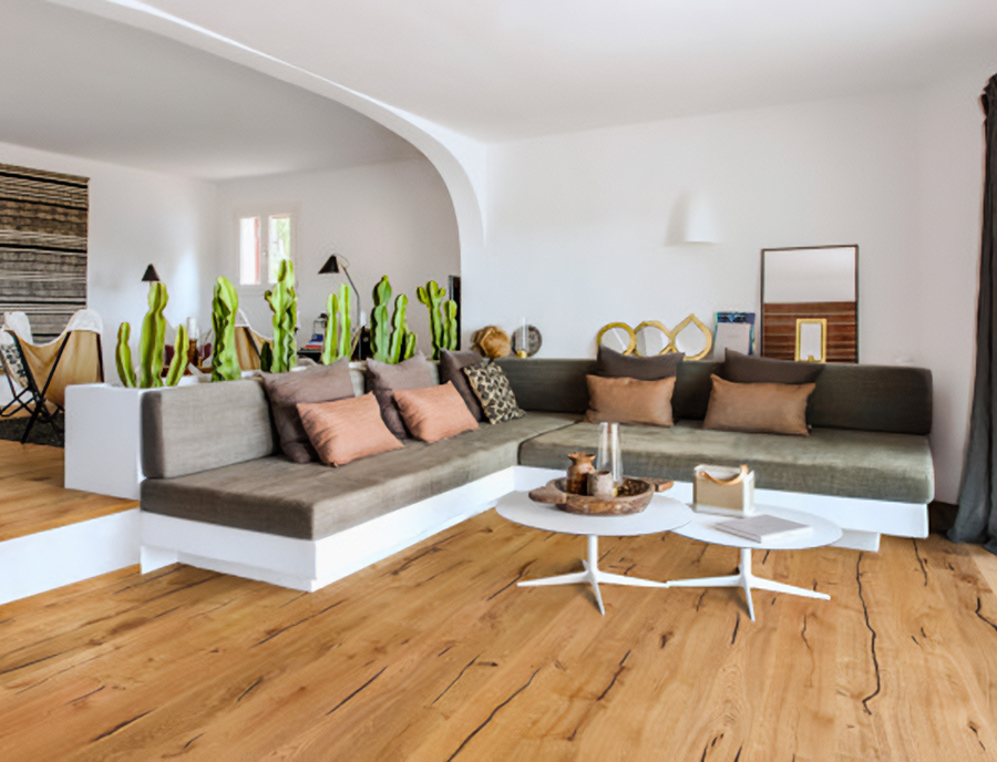 Lys og eklektisk stue med et levende eikegulv, en spesialbygd L-formet sofa utsmykket med fargerike puter, en unik bakgrunn med kaktustrykk og et moderne rundt salongbord.