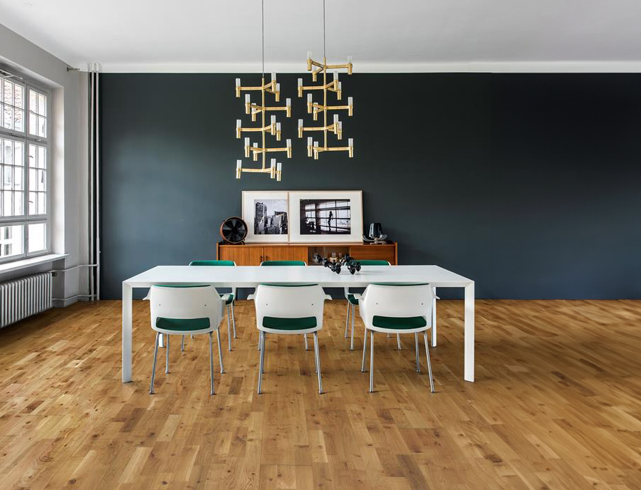 Moderne møterom med naturlig eikeparkett, et langt hvitt bord med grønne og hvite stoler, en mørk blågrønn aksentvegg og en geometrisk lysekrone.