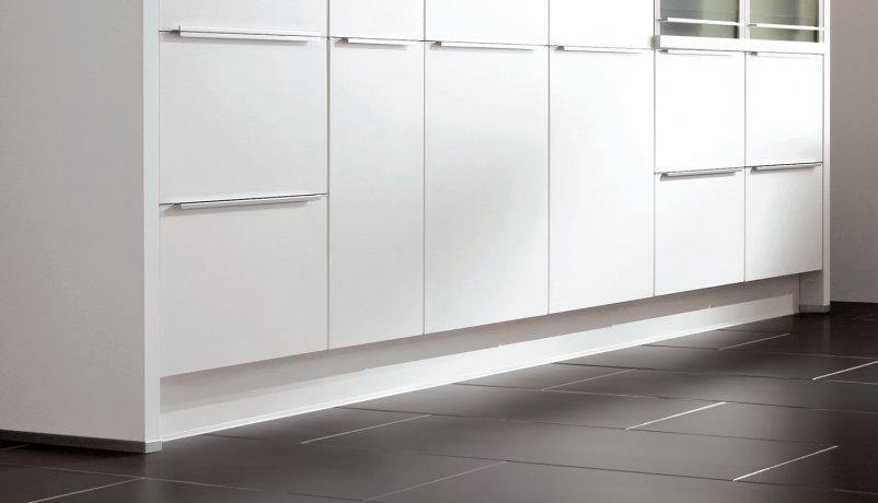 Moderne kjøkken med hvite skap og skuffer montert over en mørk flislagt gulv, med en elegant montering av lister og sokler.